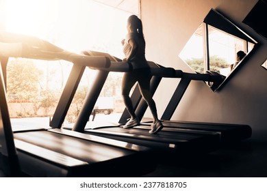 silhouette of sportswoman running on treadmill machine.  do cardio in the morning in the luxury gym room with outdoor sun views from the large windows.