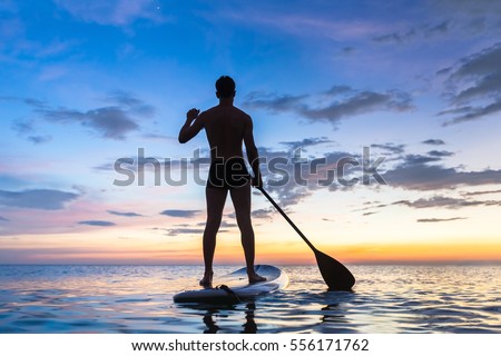 Silhouette of stand up paddle boarder paddling at sunset on a flat warm quiet sea