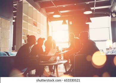 Silhouette of startup business team. Meeting on the couch. Big open space office. Five people. Intentional sun glare and lens flares