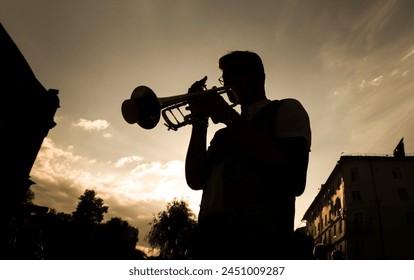 silhouette of a street musician playing the trumpet against the backdrop of the sunset sky - Powered by Shutterstock