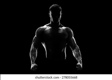 Silhouette of a strong bodybuilder. Confident young fitness man with strong hands and clenched fists. Black and white photo. Dramatic light.
