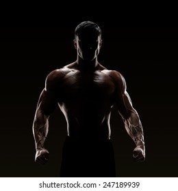 Silhouette of a strong fighter. Confident young fitness man with strong hands and clenched fists. 
