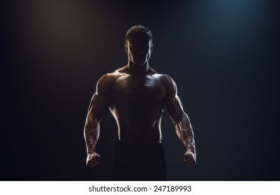 Silhouette of a strong fighter. Confident young fitness man with strong hands and clenched fists. Dramatic light.