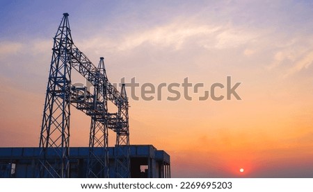 Silhouette structure of unconnected high-voltage electric pylons with cable lines and power distribution building station in construction site area at sunset time, low angle view with copy space