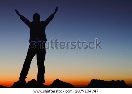 Silhouette success person raised hands on the peak of mountain with Smooth orange blue gradient of dawn sky. 