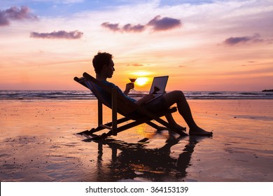Silhouette Of Successful Business Man Reading Emails On Laptop On The Beach At Sunset, Freelance Job Concept, Work Abroad