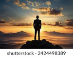 Silhouette of a successful businessman, a man in a suit, standing on top of a mountain and looking at the sunrise, on the background of rocks. Concept of competition and leadership. Copy space.