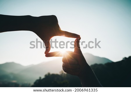 Silhouette of successful woman hands making a frame on sunrise mountain top