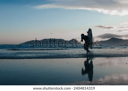 silhouette of a surfer about to enter the sea on a paradisiacal beach at sunset