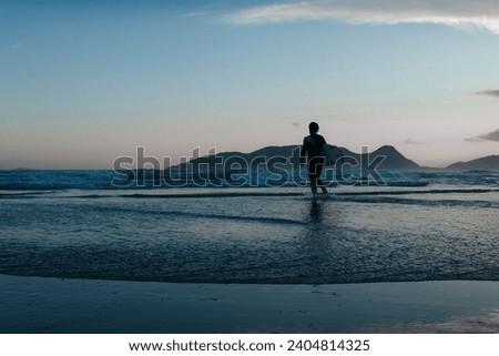 silhouette of a surfer about to enter the sea on a paradisiacal beach at sunset