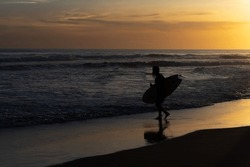 Silhouette Of Surfer Entering The Sea With His Board At Sunset.