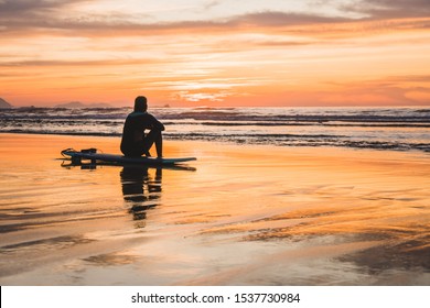 Silhouette of a surfer sitting on the beach of the Atlantic Ocean, near San Sebastian and Bilbao, North of Spain, Europe watching a dramatic stunning colorful sunset - Powered by Shutterstock