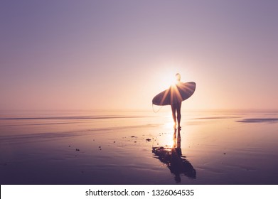 A silhouette of a surfer standing on a beach at sunset. With sun flare. Saunton, Devon, UK. - Powered by Shutterstock