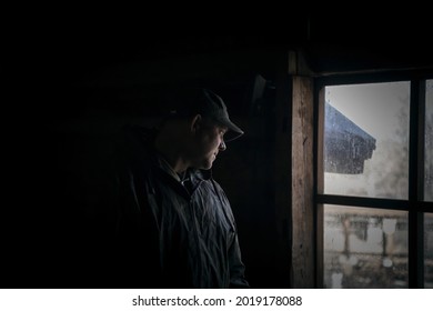 Silhouette of a suspicious strange man looking out the window in a scary dark attic of an old abandoned house in the darkness, thriller horror style