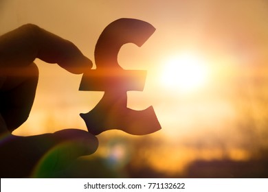 silhouette symbol of the British pound sterling in hand against the background of the dawn