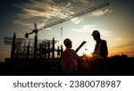 Silhouette of team engineer using laptop to control work, crane, construction site.