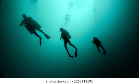 silhouette of a technical dive guide and two tourists. cenote diving, unrecognizable people