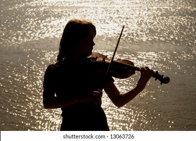 Silhouette Of Teenage Violin Player Over Sunset On River,lake Or Sea