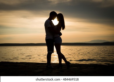 silhouette teenager lovers couple with sun between on sunset dusk sky background at the beach:black shadow hand drawn of people hug and kiss people:passion in love concept:decoration,design,valentines - Powered by Shutterstock