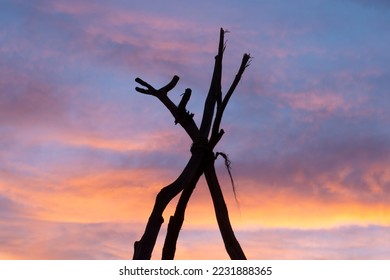 Silhouette of three branches tied together as tripod in primitive camp at sunset - Powered by Shutterstock