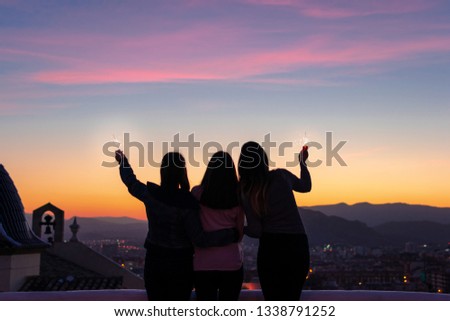 Silhouette of three girls looking to the sunset with sparkles in her hands.