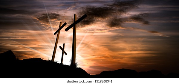 Silhouette of three wooden crosses above the hill with dramatic sky and sun rays at sunset. Religious symbol of good friday