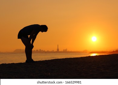 Silhouette of an tired sportsman at sunset with a city in the background - Powered by Shutterstock