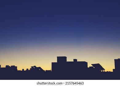 Silhouette of the top of a modern building in Madrid, Spain. Silhouette of the solar panels and chimneys located on the roof with the first rays of the sun in a yellow and blue sky.