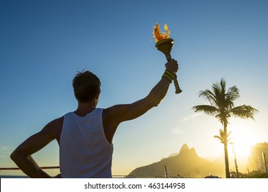 Silhouette of torchbearer athlete standing with sport torch in front of the Rio de Janeiro, Brazil sunset skyline at Ipanema Beach