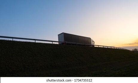 Silhouette of a truck on road at sunset.Semi truck trailer silhouette with setting sun.Delivery truck on asphalt road highway at sunset.Truck passing by a railing. Underexposed pic.