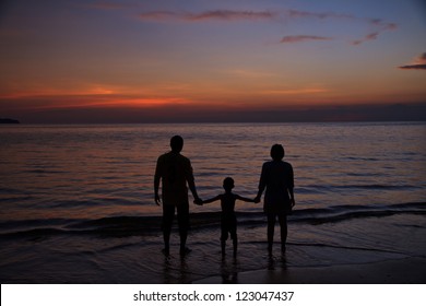 Silhouette of two adults and a child at the coast