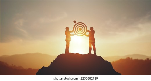 Silhouette of two businessman holding a target board on top mountain. concept of aim,  objective achievement, leadership and teamwork - Powered by Shutterstock