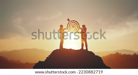 Silhouette of two businessman holding a target board on top mountain. concept of aim,  objective achievement, leadership and teamwork