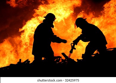 Silhouette Of Two Firemen Fighting A Huge Fire Of Burning Timber