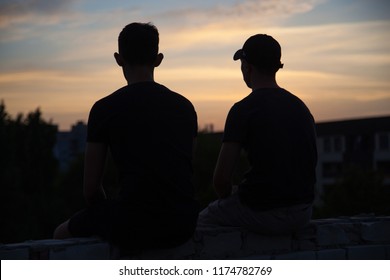silhouette of two friends sitting on the roof at sunset