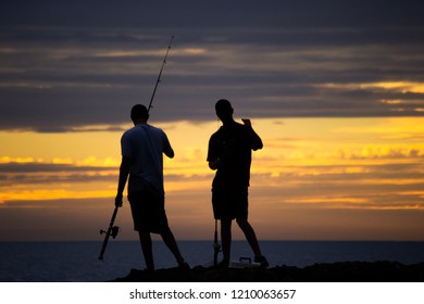 Silhouette Of Two Guys Fishing On The Beach At Sunset