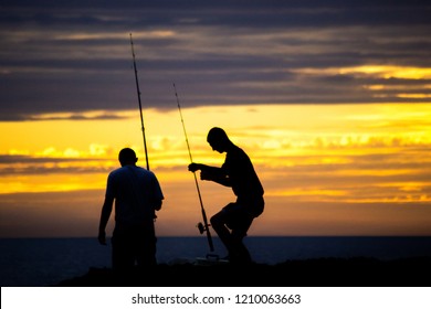 Silhouette Of Two Guys Fishing On The Beach At Sunset