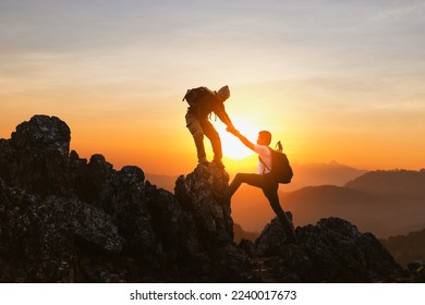 Silhouette Two Male hikers climbing up mountain cliff and one of them giving helping hand. People helping and, team work concept. - Powered by Shutterstock