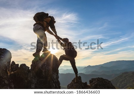 Silhouette Two Male hikers climbing up mountain cliff and one of them giving helping hand. People helping and, team work concept.