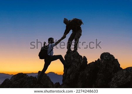 Silhouette Two Male hikers climbing up mountain cliff and one of them giving helping hand. People helping and, team work concept.