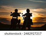 Silhouette of two motorcycle riders on the road with sunset light background.
