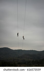 Silhouette Two People On A Zip Line Against A Cloudy Sky In Summer