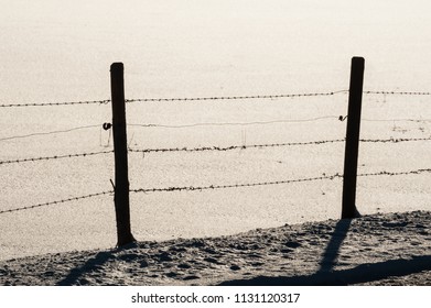 Silhouette of two posts in barbed wire fence, roughly repaired, in snow covered field