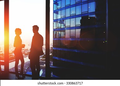 Silhouette Of A Two Successful Managing Directors Discuss Ideas After Meeting With Partners While Standing Near Big Office Window, Young Man And Woman Skilled Economists Relaxing After Conference