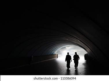 Silhouette of two woman walking into the light at the end of an underground pedestrian tunnel. - Powered by Shutterstock