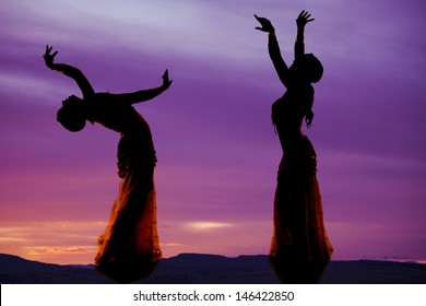 A silhouette of two women belly dancing.