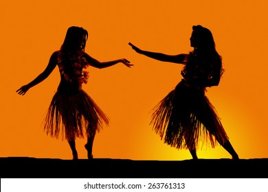 A silhouette of two women dancing in their grass skirts, in the outdoors.