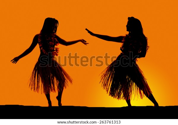 A silhouette of two women dancing in their\
grass skirts, in the\
outdoors.