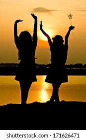 The Silhouette Of Two Young Girls Over Beautiful Twilight Sunset.