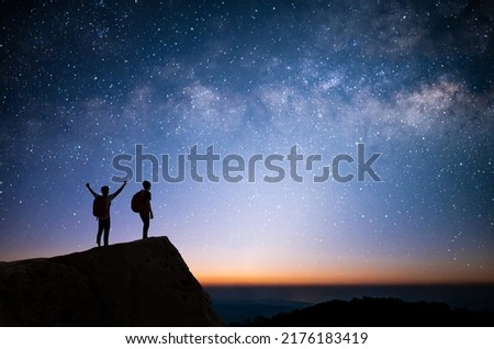 Silhouette of two young man standing, open arms and watched the star, milky way and night sky on top of the mountain. They enjoyed traveling and was successful when he reached the summit.